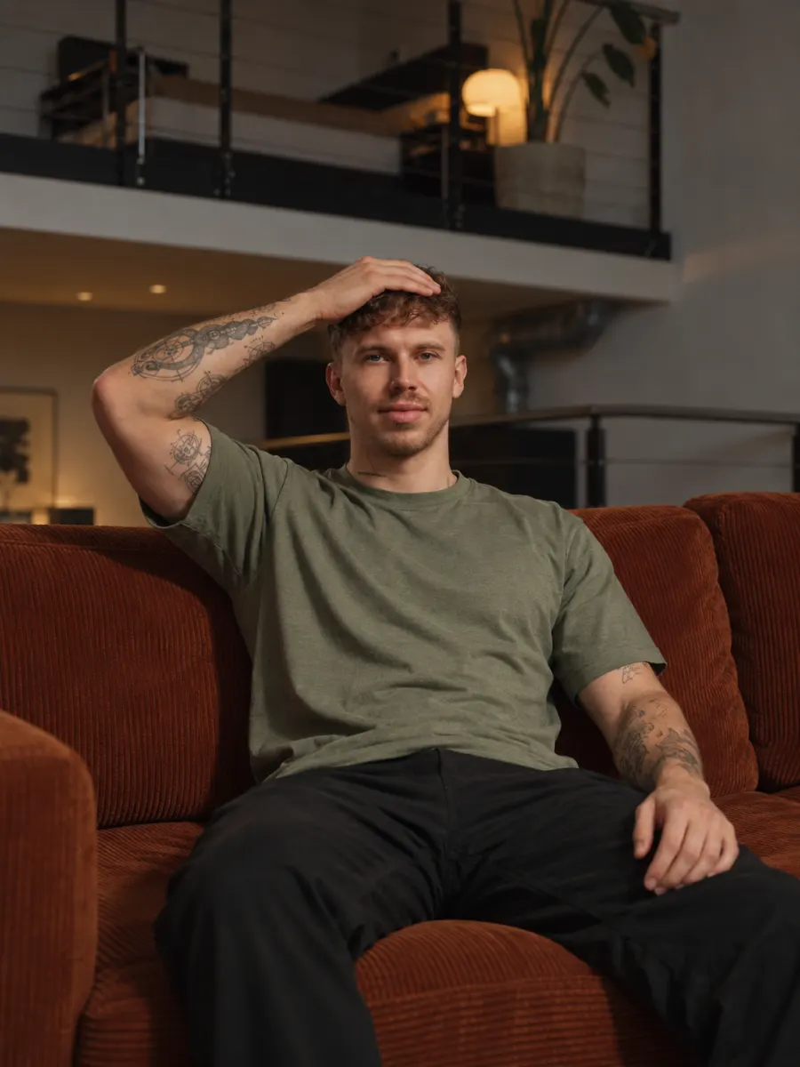 Chris sitzt abends auf der Couch und hält mit der Hand sanft gegen die Stirn.